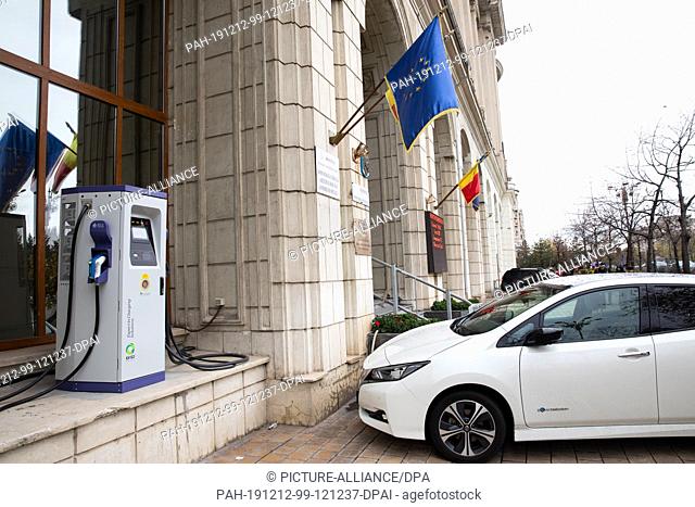 01 December 2019, Romania, Bukarest: An electric vehicle parks next to a charging station in front of a building of the Ministry of the Environment and Climate...