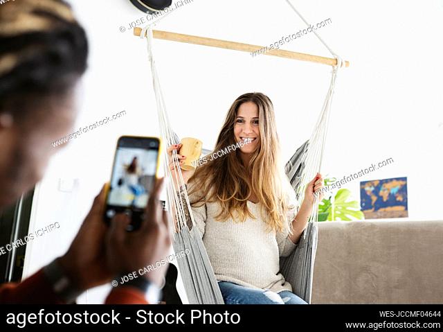 Man taking photograph of pregnant woman sitting on swing at home