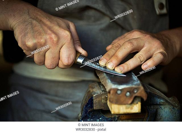 Close up of a wood carver honing the blade of a carver's knife on a leather strop, pressing the blade down, sharpening his tools