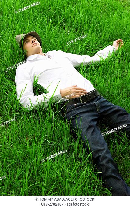 Releaxed guy laying down on the grass, facing de sky and thinking
