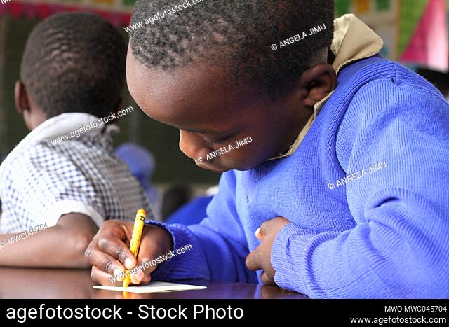 A young boy writes with a crayon at Macheke Primary School. Young learners use crayons as they learn to write. Zimbabwe
