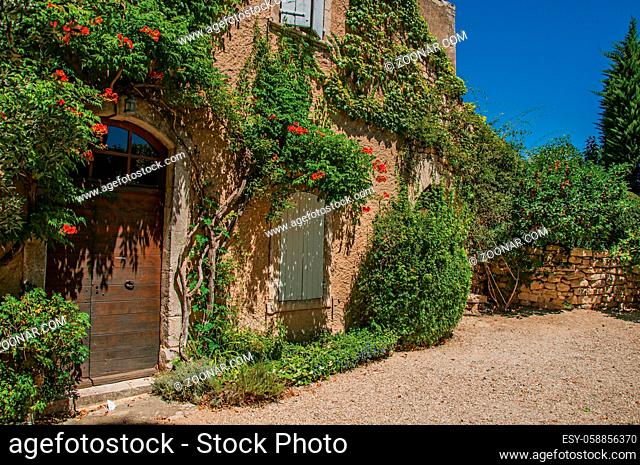 View of typical stone house facing a yard, with sunny blue sky and flowers at the village of Menerbes. In the Vaucluse department