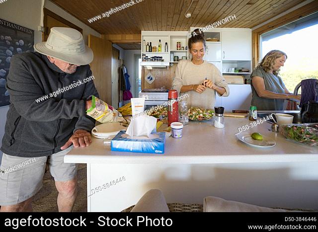 Hirtshals, Denmark A grandfather eats chips while granddaughter and daughter make dinner in the kitchen