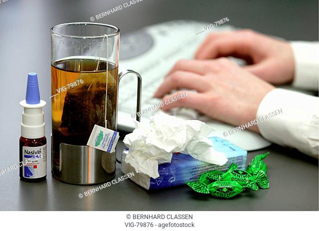 Woman in front of a computer with a cup of tea, tissues and cough sweets on his desk. Symbolic picture: To be ill at the job. - GERMANY, 29/12/2004