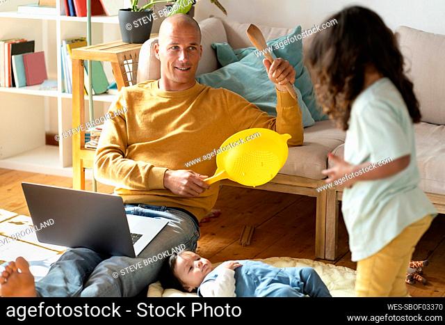 Father and daughter playing with kitchen tools while baby lying at home