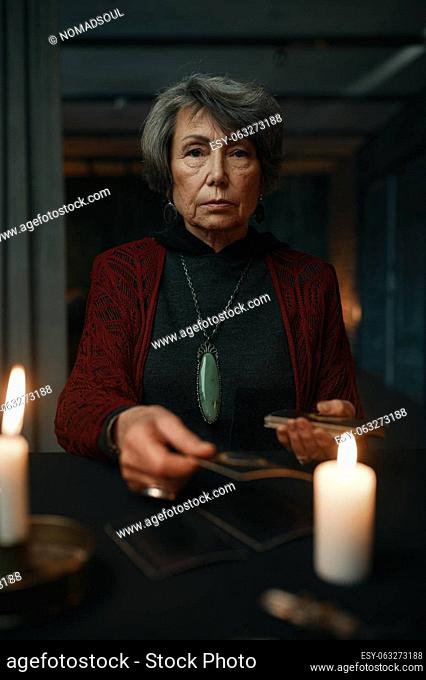 Portrait of serious confident old mature fortune teller with taro crads in dark room. Future prediction and esoteric forecast concept