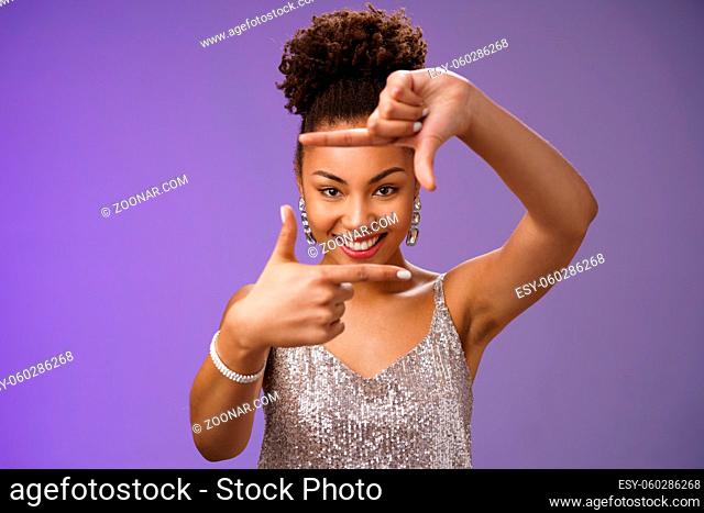 Creative good-looking african woman in silver glittering dress searching inspiration make finger frame look camera pleased smiling satisfied found perfect photo...