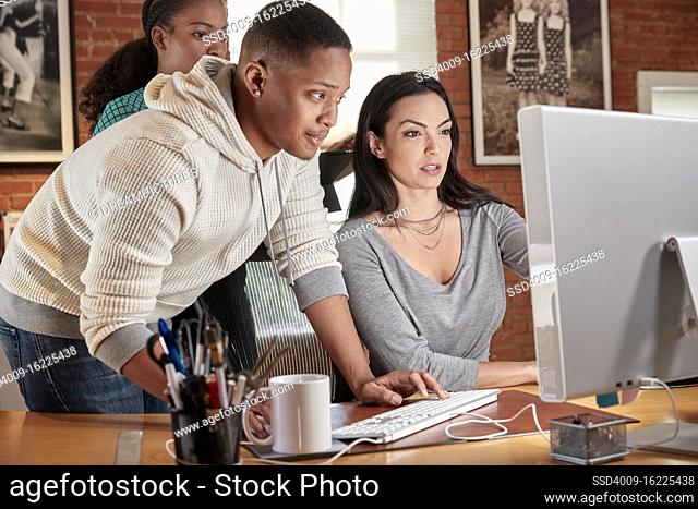 Group of young co-workers in office gathered around computer screen