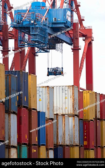 08 June 2022, Hamburg: The grab from a container gantry crane that is not in operation hangs over stacks of containers at a container terminal in Waltershof