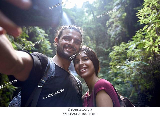 Spain, Canary Islands, La Palma, smiling couple taking a selfie in a forest