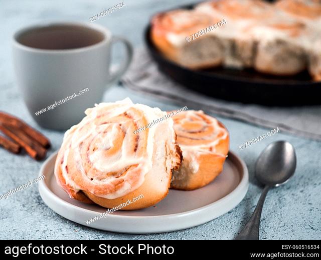 Vegan swedish cinnamon buns Kanelbullar with pumpkin spice, topping vegan cream cheese in plate with tea cup on table. Idea and recipe pastries - perfect...