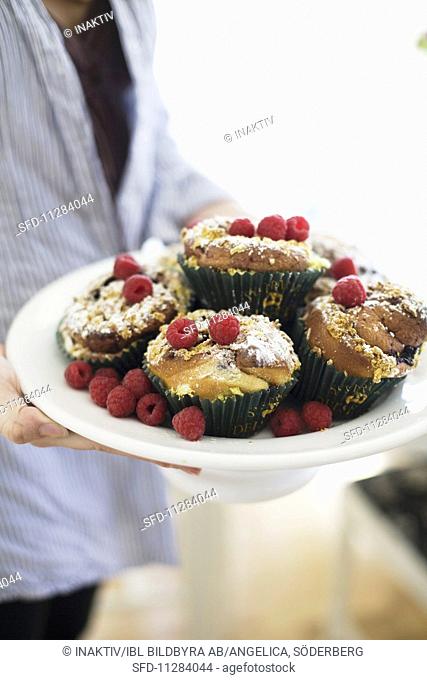 Person holding dish of muffins and fresh raspberries