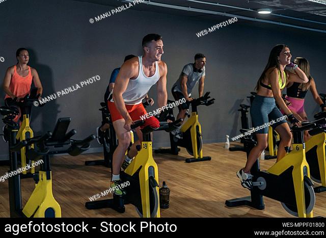 Smiling male and female athletes exercising on bike at gym