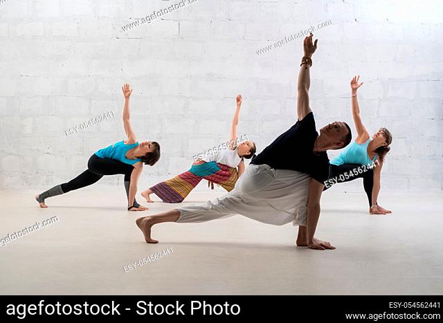 Group of people doing yoga exercises view against white brick wall