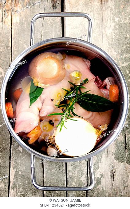 Pig's trotters in a pot with onions, bay leaves, carrots, rosemary, garlic and peppercorns