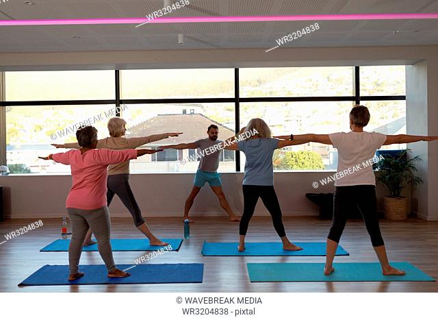 Trainer assisting senior women in performing yoga