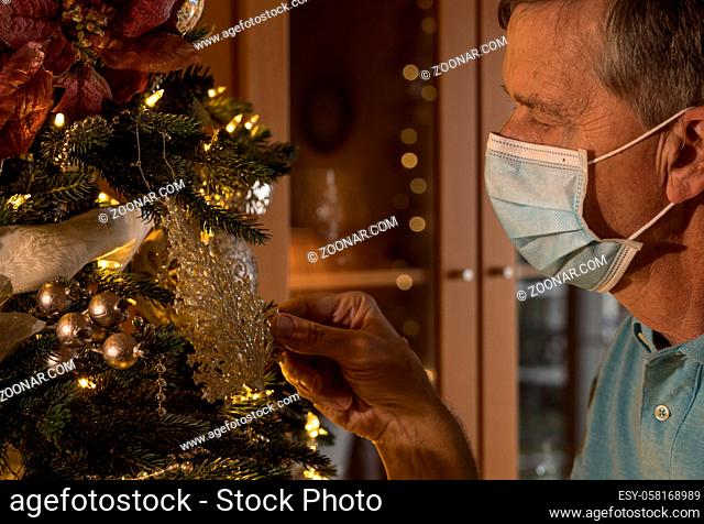 Senior adult man with christmas tree wearing medical face mask as though remembering good times before the pandemic