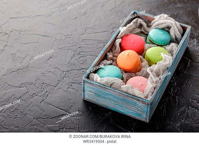 Classic French multicolored macaroon cookies in a wooden box on a black concrete background