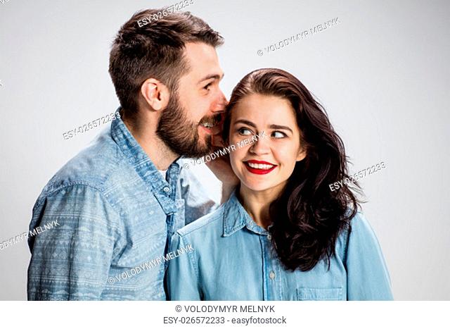 Young man whispering to woman (girlfriend) - indoor lifestyle photo on gray background