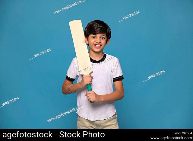 Portrait of cheerful boy standing with cricket bat against blue background