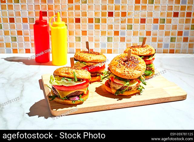Appetizing homemade burgers on wooden cutting board with bright sunlight. Burger with veal cutlets, pamidorom, cheese, red onion, lettuce