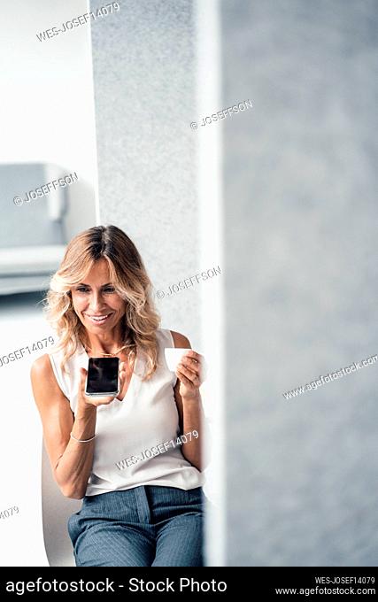 Businesswoman with coffee cup talking on speaker phone sitting at office
