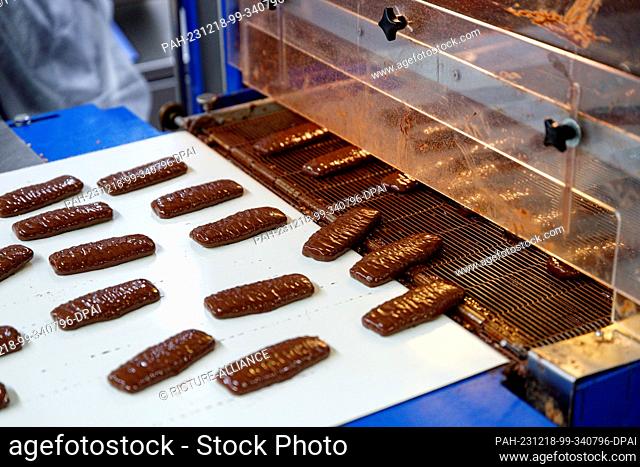 18 December 2023, North Rhine-Westphalia, Aachen: Chocolate-covered Printen come out of a machine at the Nobis Printen bakery