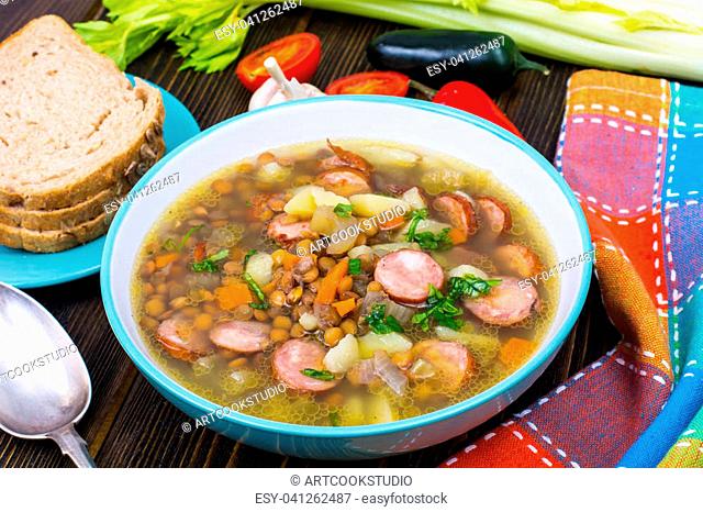 Soup with lentils, celery and sausages on old wooden table. Studio Photo