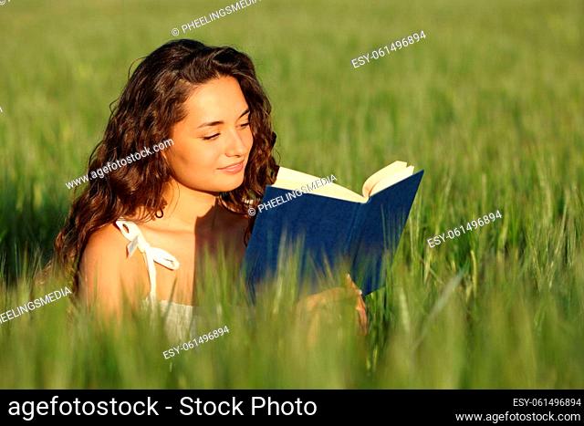 Woman reading a paper book sitting in a green wheat field