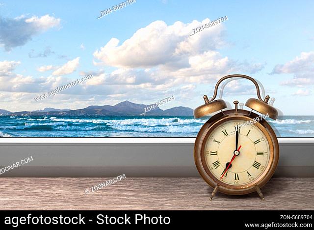 View of summer sea under blue sky from window with alarm clock