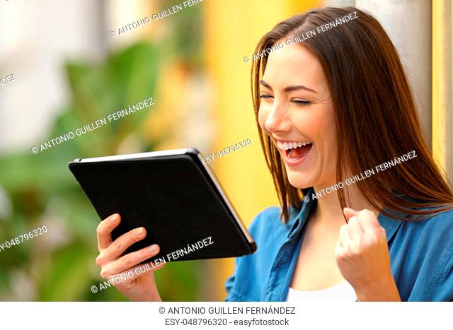 Excited woman checking online good news on tablet in the street