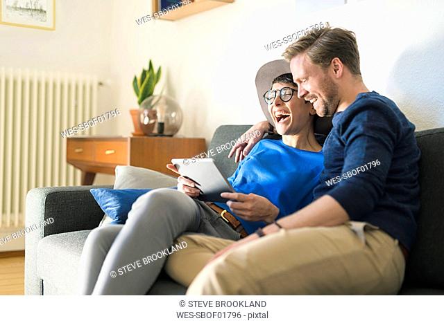 Happy casual couple relaxing on couch using tablet and laughing
