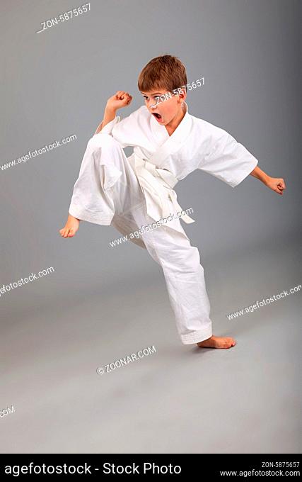Karate boy in white kimono fighting isolated on gray background