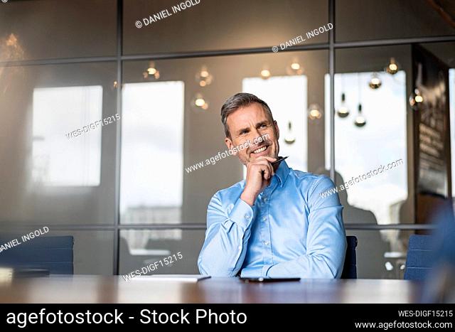 Thoughtful businessman with hand on chin looking away at work place