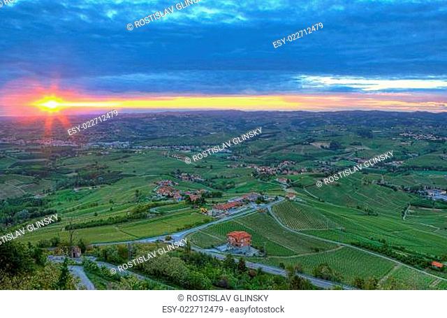 Aerial view on green hills and vineyards of Langhe under cloudy sky and rising sun early in the morning in Piedmont, Northern Italy