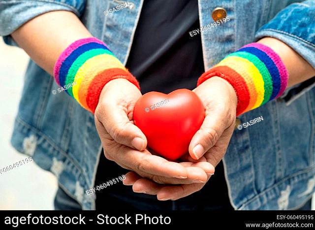 Asian lady wearing rainbow wristbands and hold red heart, symbol of LGBT pride month celebrate annual in June social of gay, lesbian, bisexual, transgender