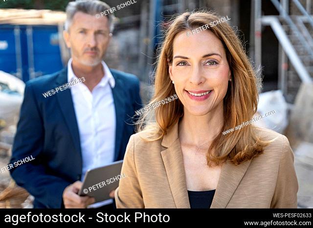 Smiling businesswoman standing with colleague in background at construction site