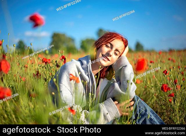 Redhead teenage girl sitting with eyes closed in poppy field on sunny day