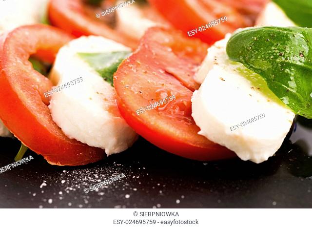 Caprese salad with mozzarella, tomato, basil and balsamic vinegar arranged on black plate