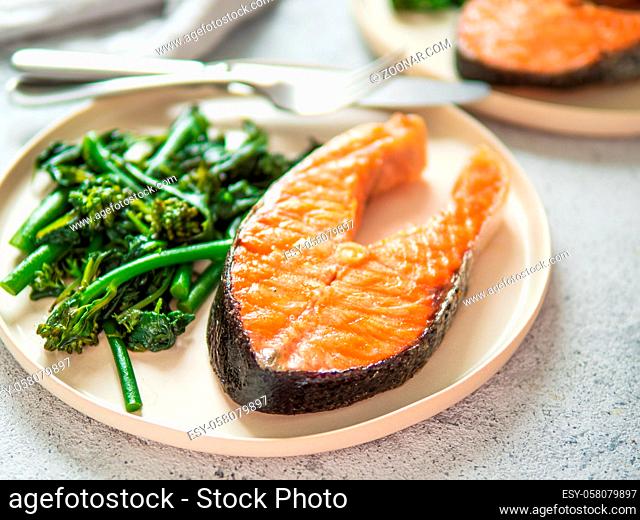 Ready-to-eat grilled salmon steak and greens - baby broccoli or broccolini and spinach on rustic craft plate over gray background. Keto diet dish