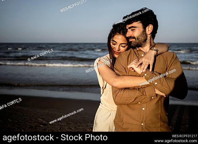 Smiling girlfriend embracing boyfriend from behind at beach