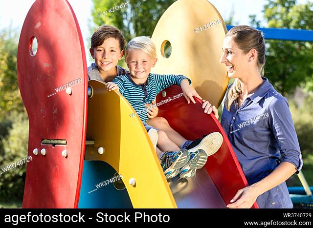 Happy family playing on adventure playground, children chuting chute