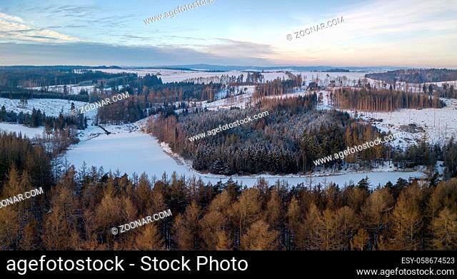 Aerial bird view of beautiful winter landscape with frozen water reservoir situated in forest covered with snow. European countryside