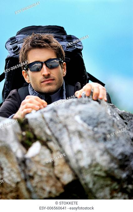 Young mountain climber with sunglasses scaling a cliff, focus on face