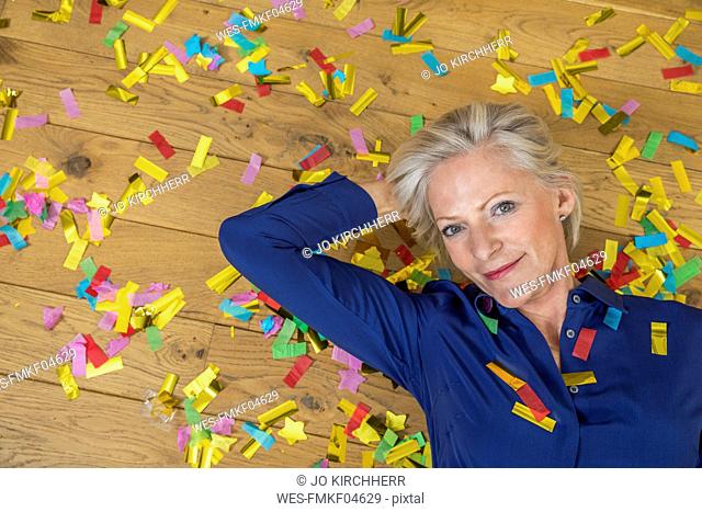 Portrait of smiling senior woman lying on floor covered with confetti