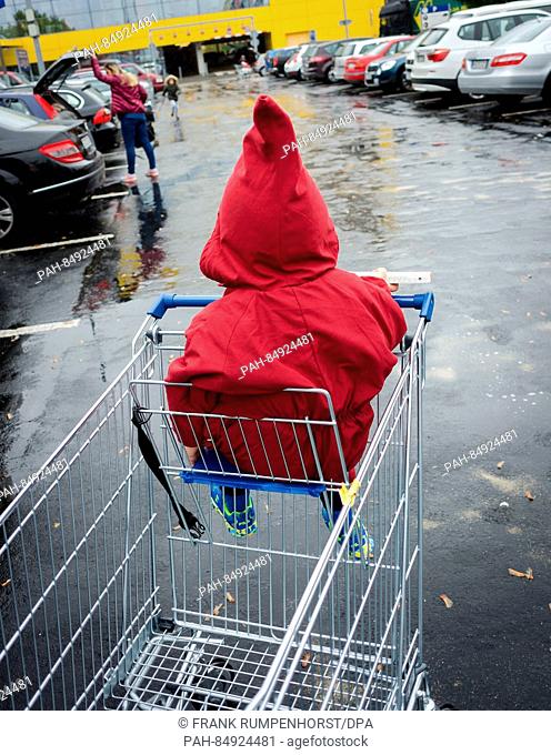 A young boy wearing his hood while waiting for his mother in the children's seat of a shopping cart during rainy weather in Frankfurt/Main, Germany