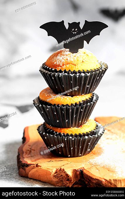 Halloween pumpkin muffins in black capsules decorated with cardboard bats. Festive Halloween cupcakes. Close-up view of delicious spooky halloween muffins on...