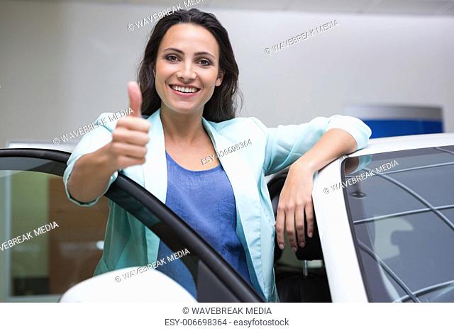 Smiling customer leaning on car while giving thumbs up