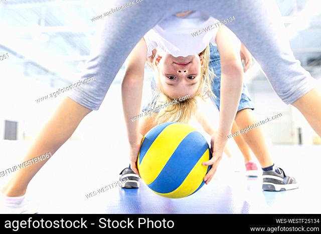 Smiling schoolgirl exercising with ball at sports court