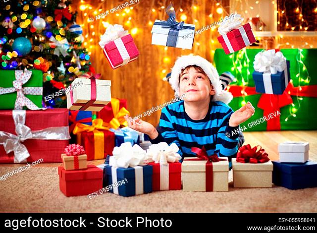 Boy lying on the floor with presents near christmas tree. Child in red hat at home in winter